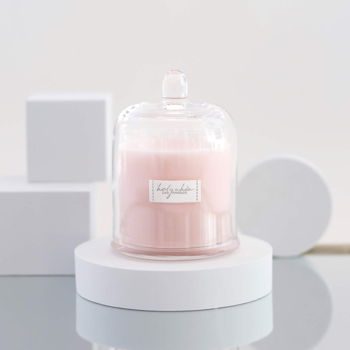 Pale pink scented candle in a clear glass container with a cloche